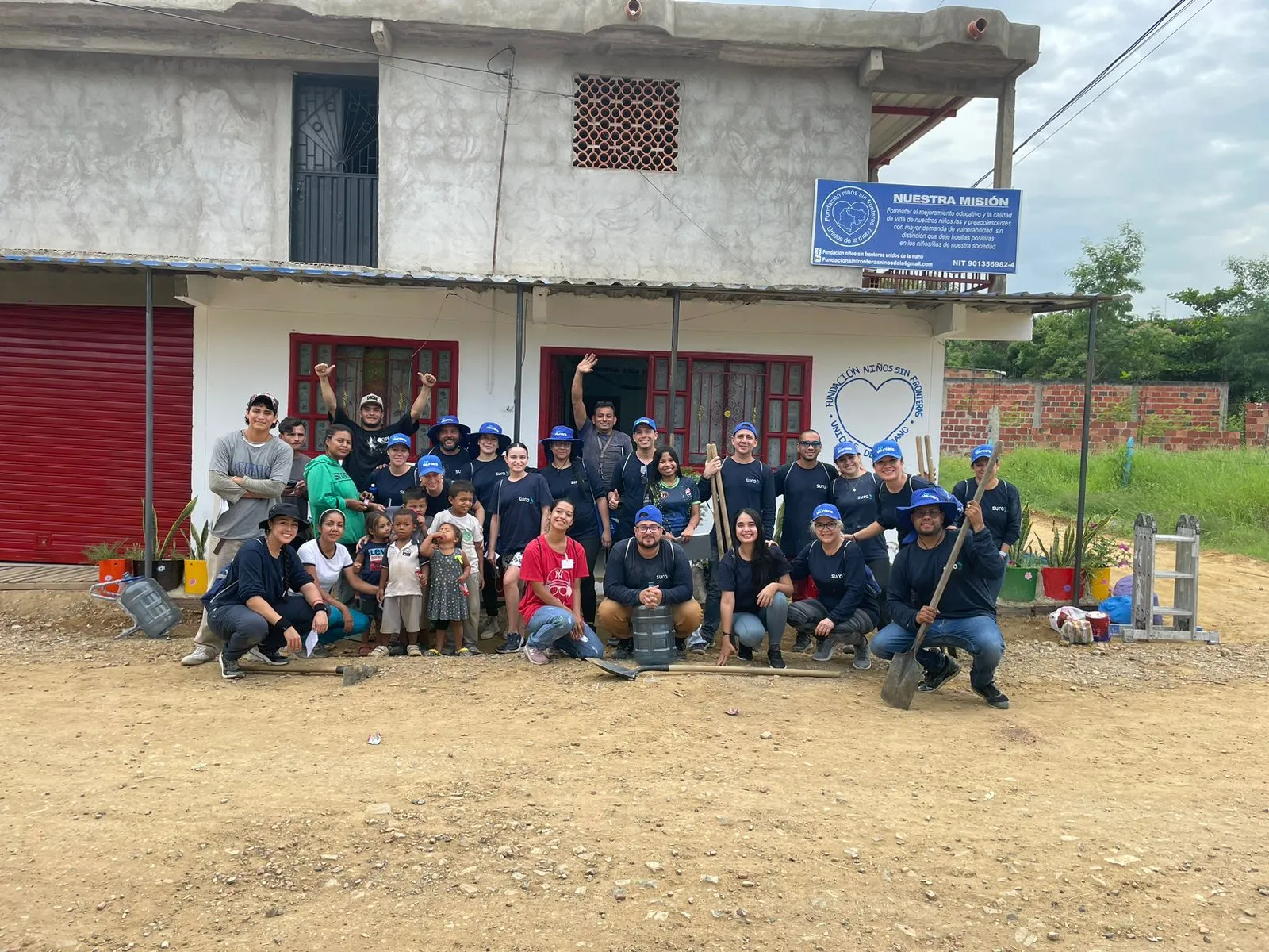 Grupo numeroso de participantes de un programa comunitario posando frente a una sede en zona rural.